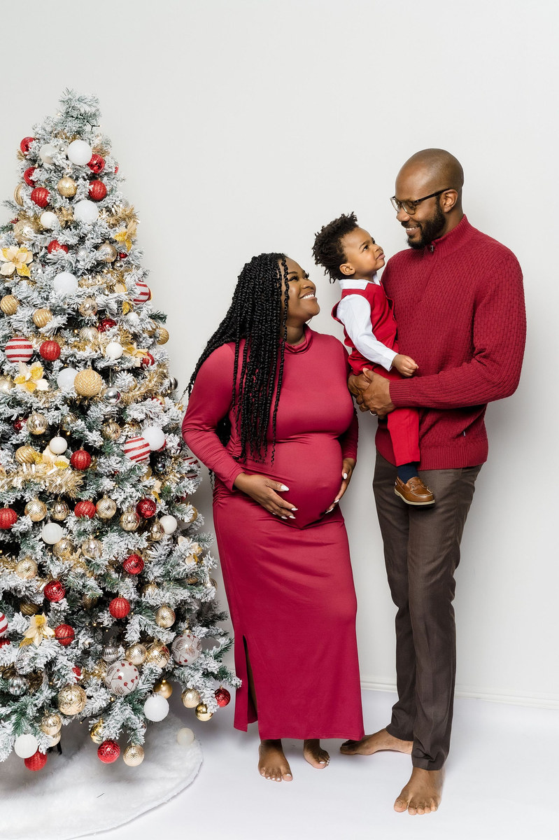 Family in red standing beside a Christmas tree, the father holding a toddler