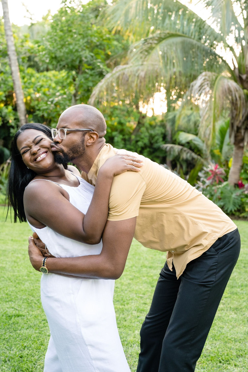Man kissing a laughing woman on the cheek in a tropical garden