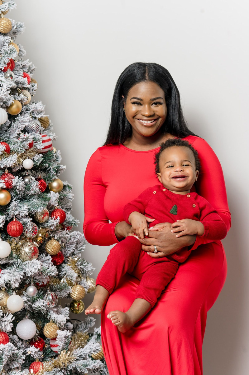 Woman in a red dress holding a laughing baby beside a Christmas tree
