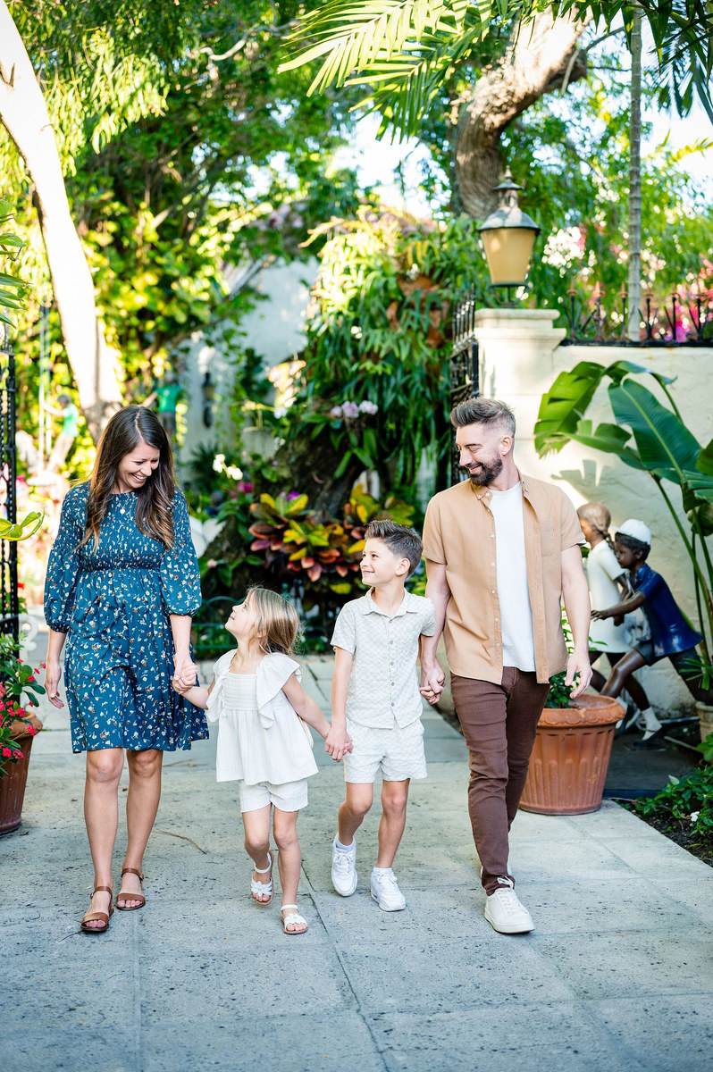 Family of four walking hand in hand along a tropical garden path