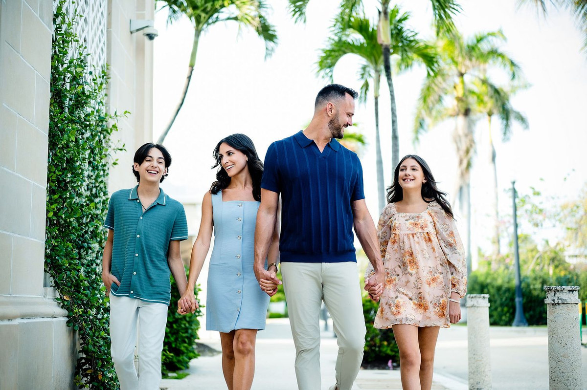 Family of four walking together past palm trees