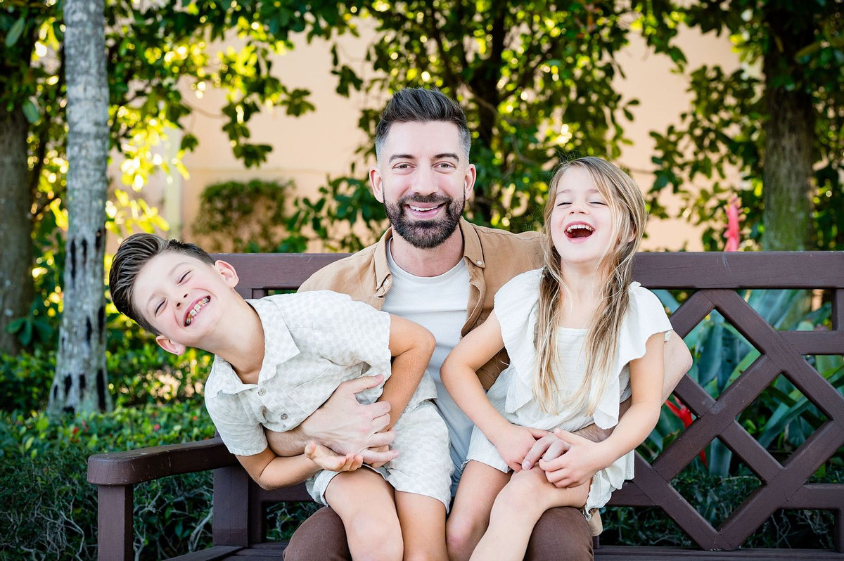Man and two children laughing together on a garden bench
