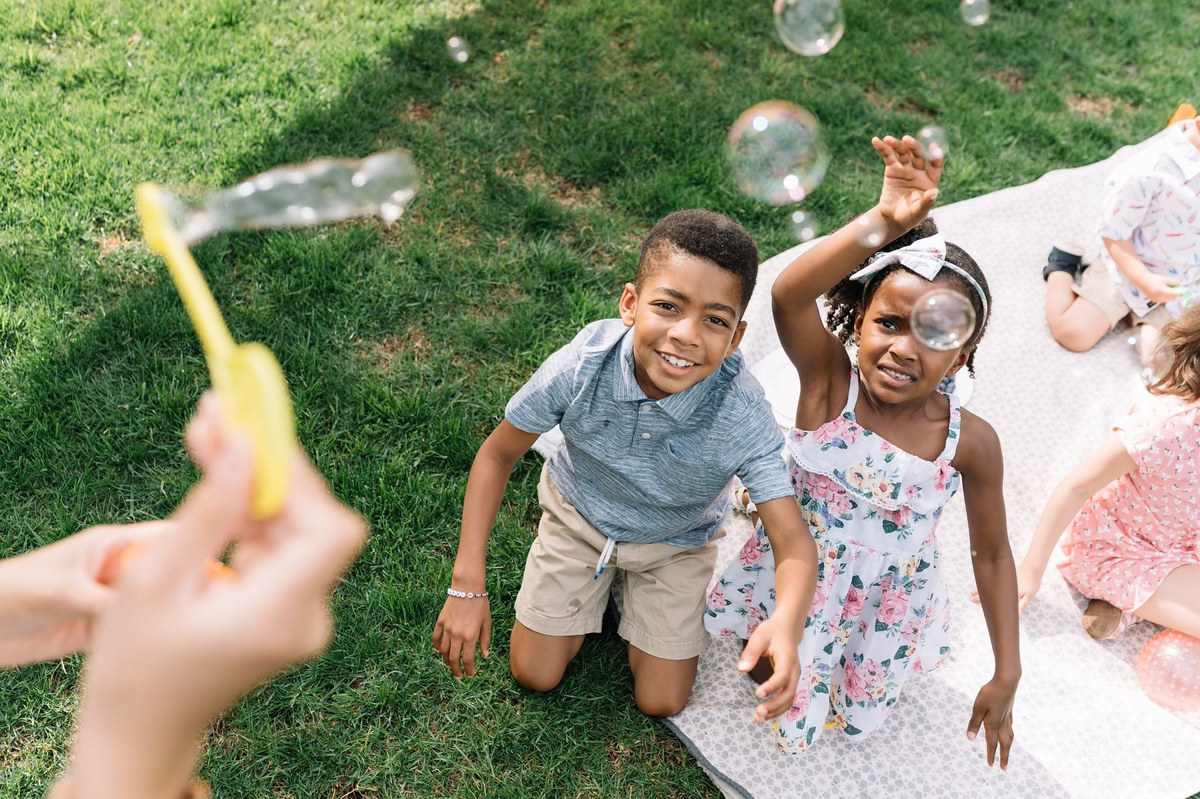 Children chasing bubbles on a lawn