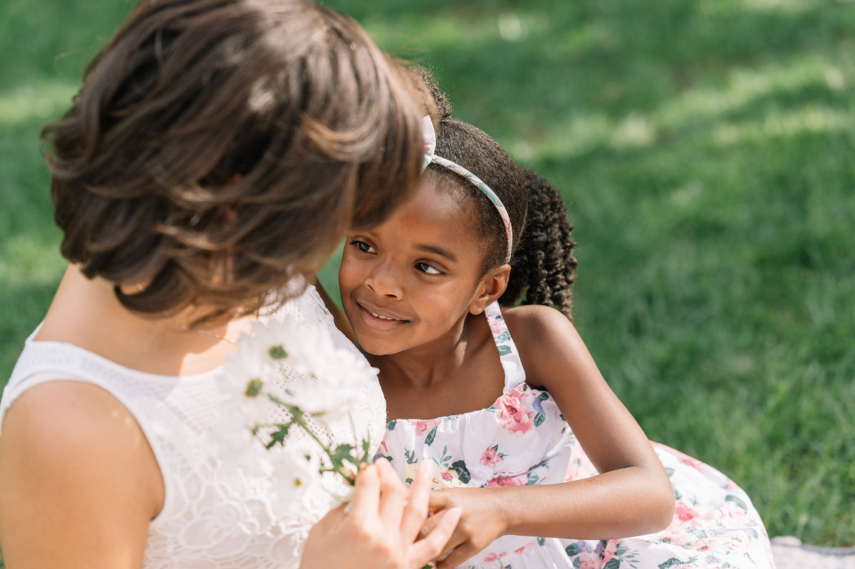 Two young girls sharing a flower on the grass