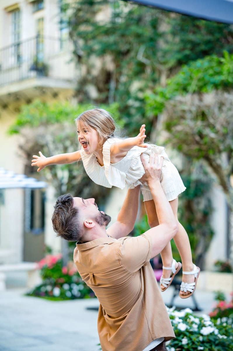 Man lifting a laughing young girl into the air on a garden path