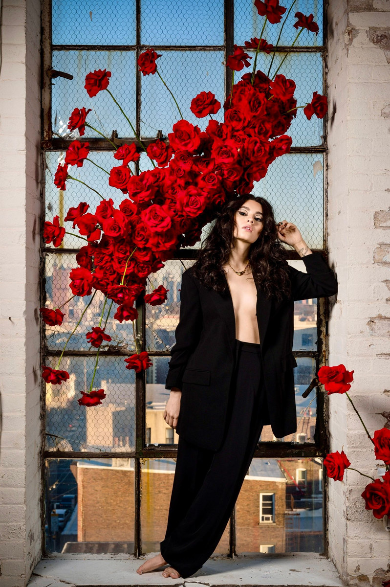 Woman in a black suit standing in a tall window framed by red roses